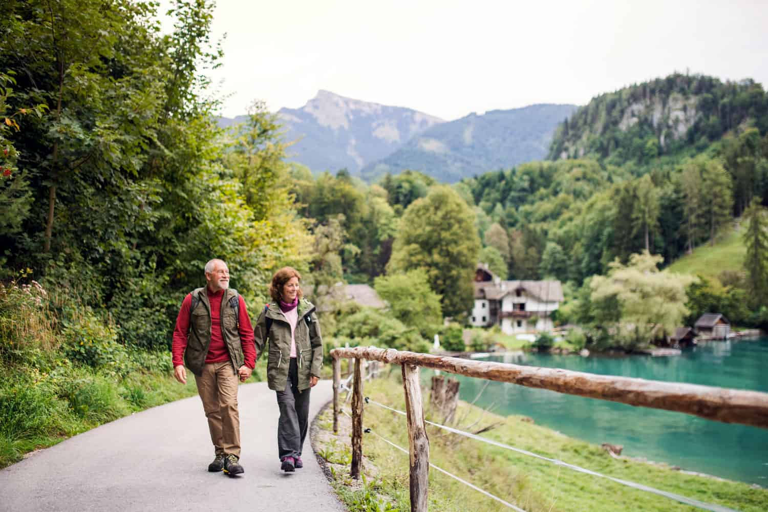 Retired couple happily walking on path near water in the mountains