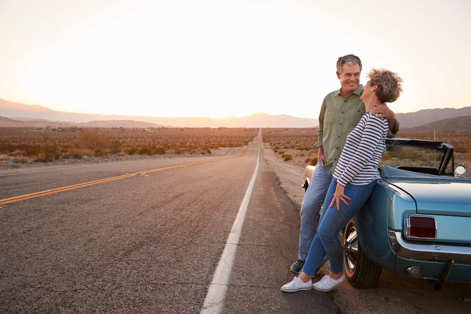 Happy couple leaning against car on highway