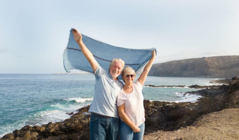Retired couple waving blanket in air at beach