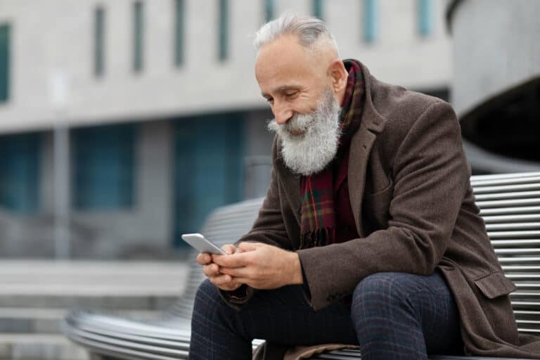 Happy elderly man using smartphone while resting on street