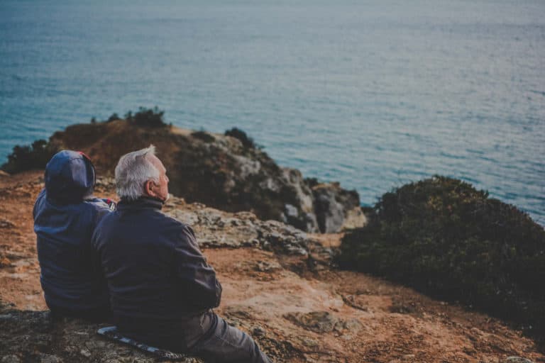 Retired couple happily looking at a lake while sitting on a hill