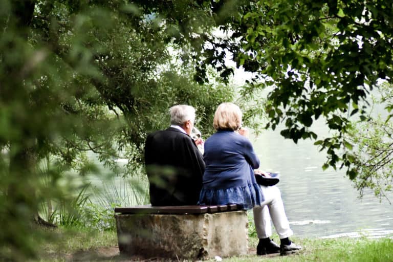 Retired couple drinking wine while sitting by the water