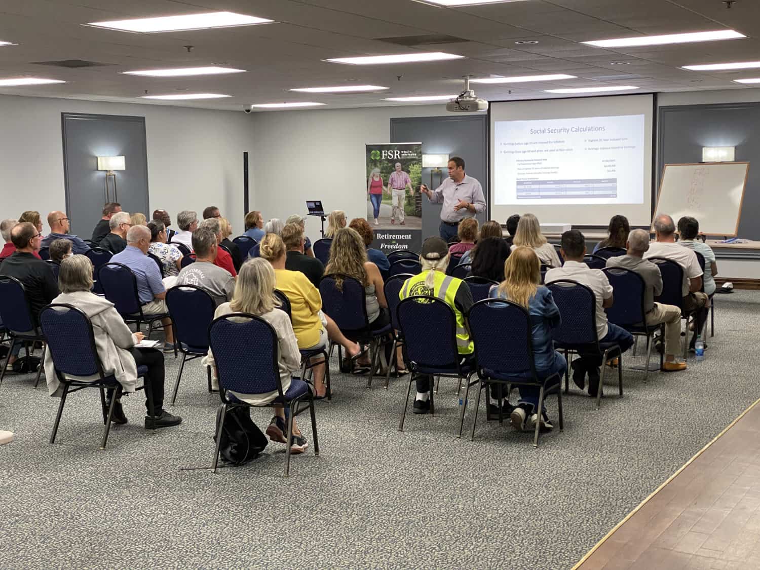 A group of people in a room listening to a presentation.